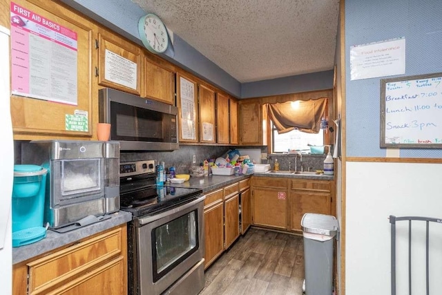 402 W Converse St, Weimar, TX 78962 - kitchen with stainless steel appliances, brown cabinets, a textured ceiling, and wood finished floors