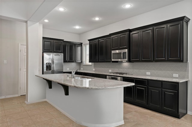 4831 Sunset Park Ln, Rosharon, TX 77583 - kitchen featuring appliances with stainless steel finishes, dark cabinetry, decorative backsplash, light stone countertops, and a breakfast bar
