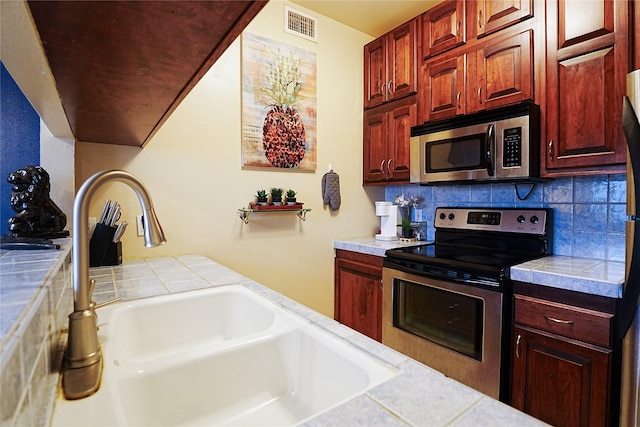 4004 Montrose Blvd Unit 45A, Houston, TX 77006 - kitchen with stainless steel appliances, tasteful backsplash, tile countertops, and reddish brown cabinets