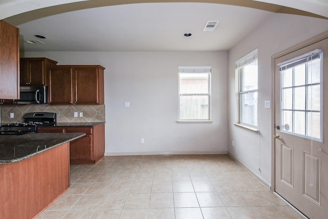 6533 Gray Birch Ln, Dickinson, TX 77539 - kitchen with black gas range, stainless steel microwave, decorative backsplash, dark stone countertops, and light tile patterned flooring