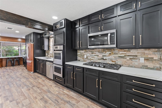 13855 Lantern Ln, Houston, TX 77015 - kitchen with stainless steel appliances, dark cabinets, tasteful backsplash, light wood-style floors, and recessed lighting