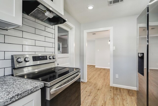 2003 Amelia St, Baytown, TX 77520 - kitchen with electric stove, wall chimney exhaust hood, light wood-style flooring, white cabinetry, and light stone countertops