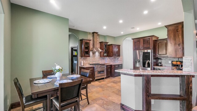 1804 Esther Dr, Houston, TX 77088 - kitchen with stainless steel appliances, wall chimney range hood, arched walkways, dark brown cabinetry, and light countertops