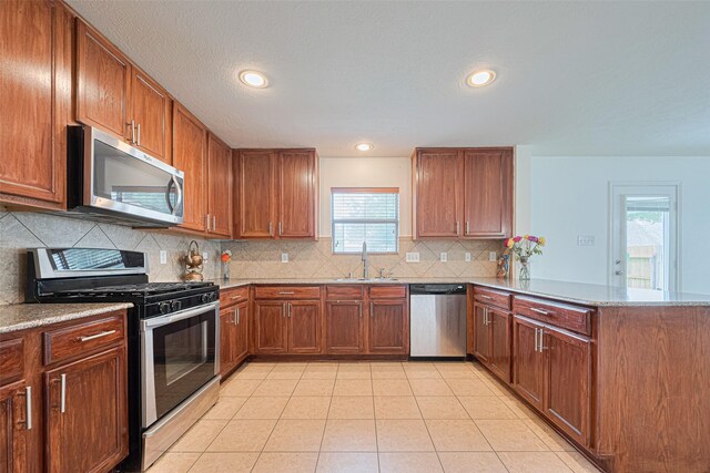 18231 Rexine Ln, Cypress, TX 77433 - kitchen featuring appliances with stainless steel finishes, a peninsula, decorative backsplash, brown cabinetry, and recessed lighting