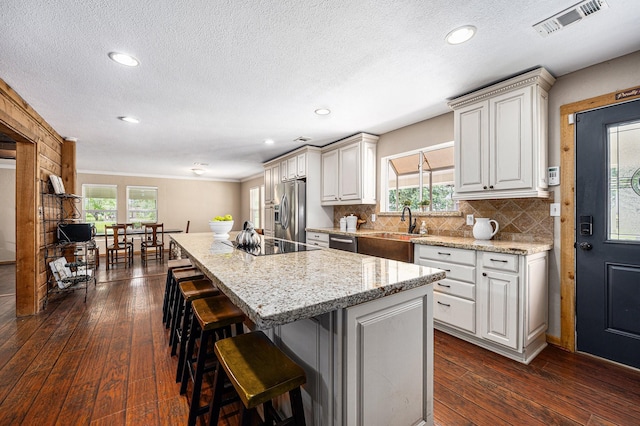 7403 Falcon Dr, Brookshire, TX 77423 - kitchen featuring stainless steel appliances, a kitchen island, a breakfast bar area, dark wood finished floors, and light stone countertops