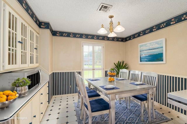 1311 Linwood Dr, Wharton, TX 77488 - dining area with a wainscoted wall, wallpapered walls, a chandelier, light flooring, and a textured ceiling