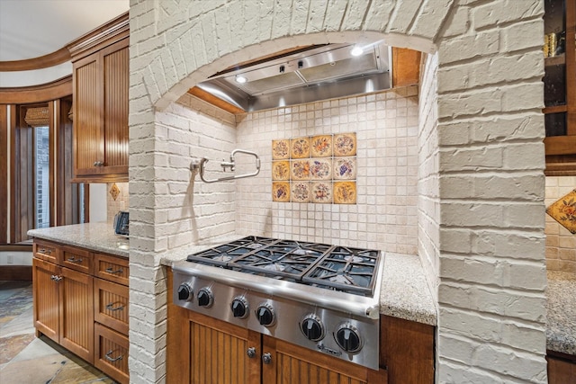 4132 Coleridge St, Houston, TX 77005 - kitchen with stainless steel gas stovetop, wall chimney range hood, light stone countertops, and brown cabinets