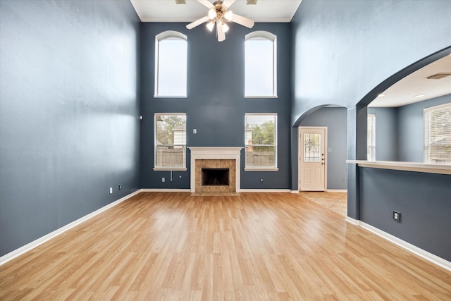 20202 Windsor Trace Ln, Richmond, TX 77407 - unfurnished living room with a ceiling fan, light wood-style floors, healthy amount of natural light, a fireplace with flush hearth, and a towering ceiling