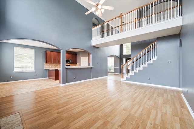 20202 Windsor Trace Ln, Richmond, TX 77407 - unfurnished living room with arched walkways, a towering ceiling, a ceiling fan, light wood-style flooring, and stairs