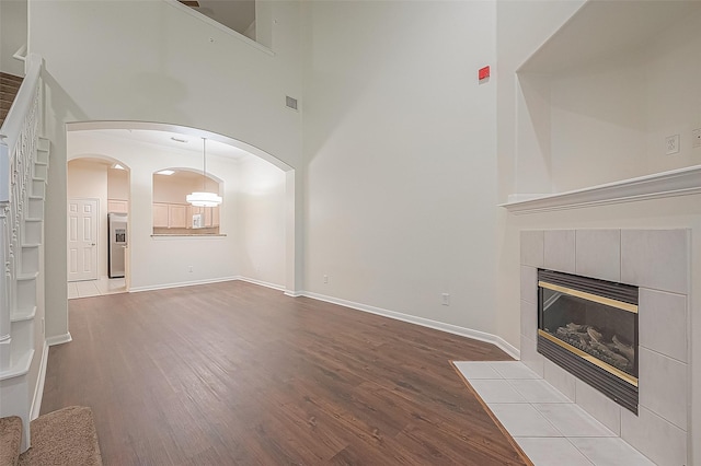 2710 Grants Lake Blvd Unit T6, Sugar Land, TX 77479 - unfurnished living room featuring wood finished floors, a tile fireplace, arched walkways, and a towering ceiling