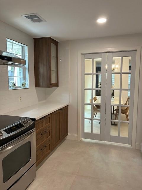 1635 Chippendale Rd, Houston, TX 77018 - kitchen featuring stainless steel electric range, light countertops, glass insert cabinets, wall chimney exhaust hood, and recessed lighting