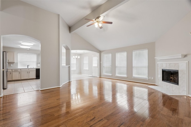 16306 Ancient Forest Dr, Humble, TX 77346 - unfurnished living room with a ceiling fan, arched walkways, a tile fireplace, beamed ceiling, and light wood-style flooring
