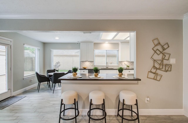 22523 Wildwood Grove Dr, Katy, TX 77450 - kitchen featuring dark countertops, a breakfast bar area, white cabinets, backsplash, and crown molding