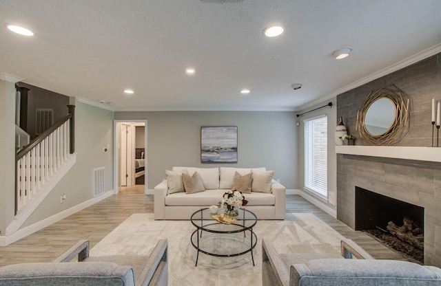 22523 Wildwood Grove Dr, Katy, TX 77450 - living room featuring light wood-type flooring, crown molding, recessed lighting, stairs, and a tiled fireplace