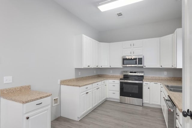 575 Hartman Rd, Silsbee, TX 77656 - kitchen with stainless steel appliances, light wood-type flooring, and white cabinetry