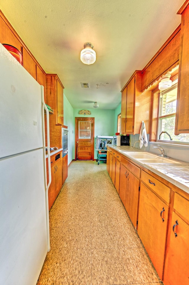 1726 Wilde Rock Way, Houston, TX 77018 - kitchen featuring freestanding refrigerator, light countertops, brown cabinetry, and light flooring