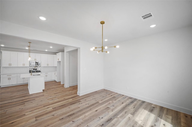 19219 Hikers Trail Dr, Humble, TX 77346 - kitchen with appliances with stainless steel finishes, white cabinets, light countertops, a center island with sink, and light wood finished floors