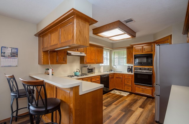 3701 Regency Dr, Deer Park, TX 77536 - kitchen with black appliances, a peninsula, under cabinet range hood, and brown cabinets