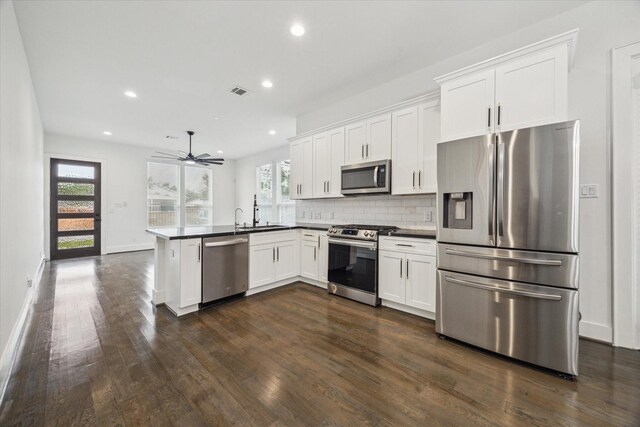 1825 Northwood Dr, Houston, TX 77009 - kitchen featuring appliances with stainless steel finishes, dark wood-type flooring, dark countertops, a peninsula, and white cabinetry
