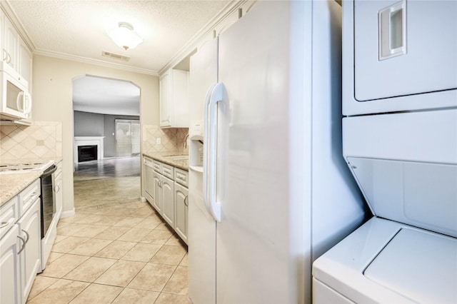 12550 Whittington Dr Unit 816, Houston, TX 77077 - kitchen featuring white appliances, stacked washer / dryer, arched walkways, tasteful backsplash, and white cabinetry