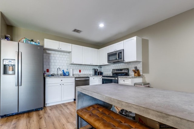 8206 Bassett St, Houston, TX 77051 - kitchen featuring appliances with stainless steel finishes, white cabinets, light wood-style floors, and recessed lighting
