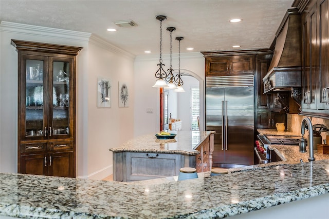 12042 Bolero Point Ln, Houston, TX 77041 - kitchen featuring premium appliances, premium range hood, light stone countertops, dark brown cabinetry, and hanging light fixtures