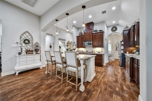6507 Crystal Forest Trl, Katy, TX 77493 - kitchen with arched walkways, stainless steel appliances, a kitchen island, dark brown cabinetry, and a kitchen breakfast bar