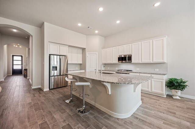 20923 Bradley Gardens Dr, Spring, TX 77379 - kitchen with appliances with stainless steel finishes, white cabinets, a kitchen island with sink, a breakfast bar, and light stone counters