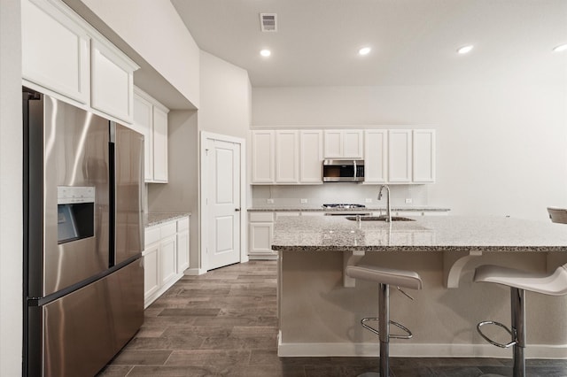 20923 Bradley Gardens Dr, Spring, TX 77379 - kitchen featuring appliances with stainless steel finishes, white cabinets, dark wood-type flooring, light stone counters, and a kitchen island with sink