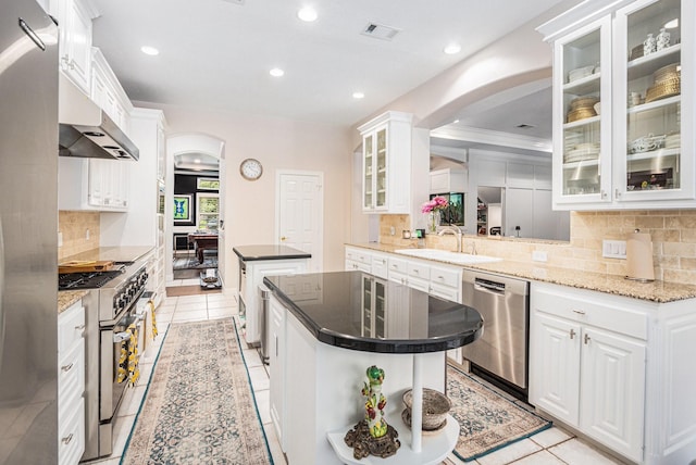 4925 Pine St, Bellaire, TX 77401 - kitchen featuring appliances with stainless steel finishes, a kitchen island, under cabinet range hood, arched walkways, and tasteful backsplash