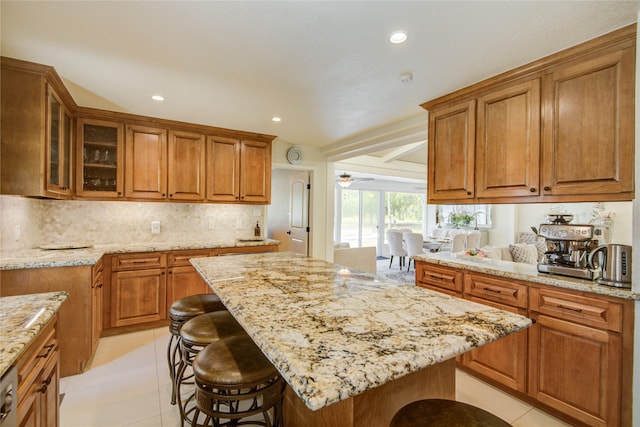 14227 Indian Wells Dr, Houston, TX 77069 - kitchen with a kitchen breakfast bar, light stone counters, brown cabinets, glass insert cabinets, and tasteful backsplash