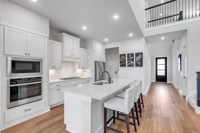 9219 Trimble Landing Dr, Tomball, TX 77375 - kitchen with appliances with stainless steel finishes, decorative backsplash, an island with sink, light stone countertops, and light wood finished floors