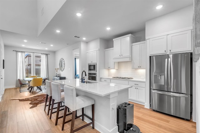 9219 Trimble Landing Dr, Tomball, TX 77375 - kitchen featuring stainless steel appliances, tasteful backsplash, light wood-type flooring, a breakfast bar, and white cabinetry