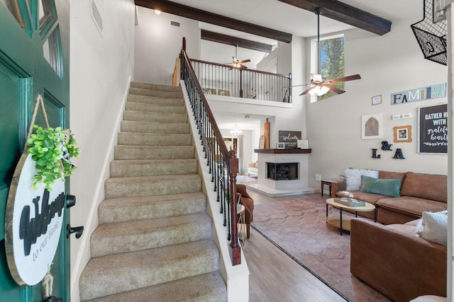 248 S Pathfinders Cir, The Woodlands, TX 77381 - stairs featuring a ceiling fan, a fireplace with raised hearth, wood finished floors, beam ceiling, and a towering ceiling