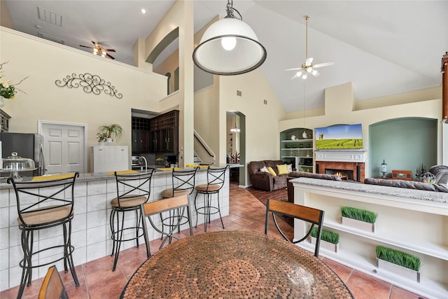 17706 Riata Lake Dr, Cypress, TX 77433 - kitchen with a ceiling fan, high vaulted ceiling, a breakfast bar area, freestanding refrigerator, and a lit fireplace