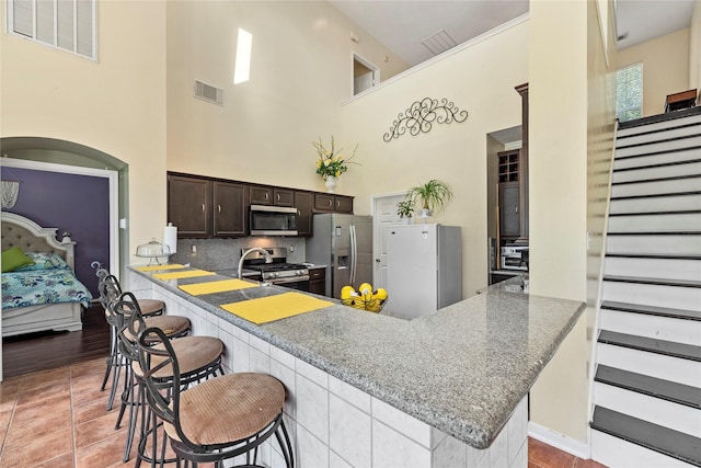 17706 Riata Lake Dr, Cypress, TX 77433 - kitchen featuring stainless steel appliances, dark brown cabinetry, a peninsula, a kitchen bar, and a high ceiling