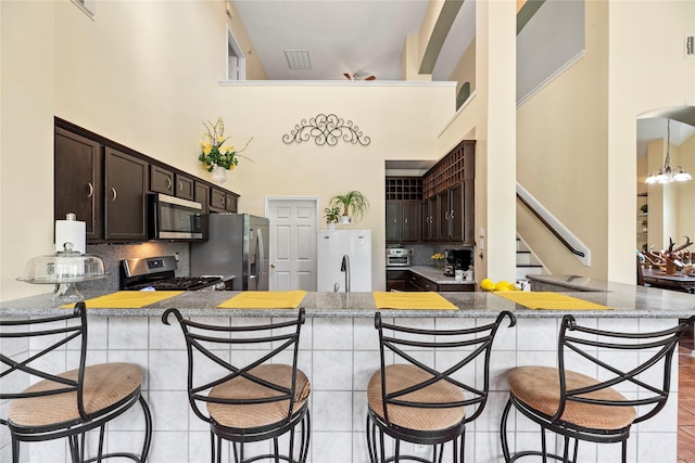 17706 Riata Lake Dr, Cypress, TX 77433 - kitchen with appliances with stainless steel finishes, a towering ceiling, dark brown cabinets, decorative backsplash, and a kitchen breakfast bar