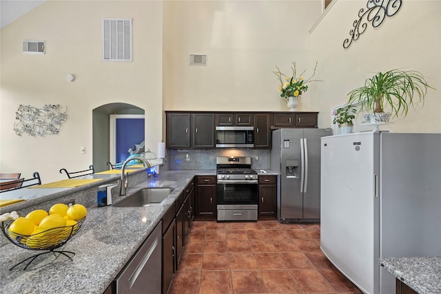 17706 Riata Lake Dr, Cypress, TX 77433 - kitchen featuring appliances with stainless steel finishes, high vaulted ceiling, arched walkways, light stone counters, and dark brown cabinets