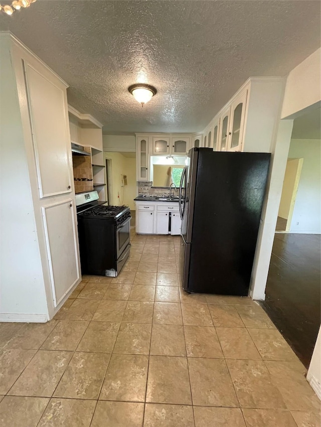 7539 Carothers St, Houston, TX 77028 - kitchen featuring stainless steel appliances, dark countertops, glass insert cabinets, light tile patterned flooring, and a textured ceiling