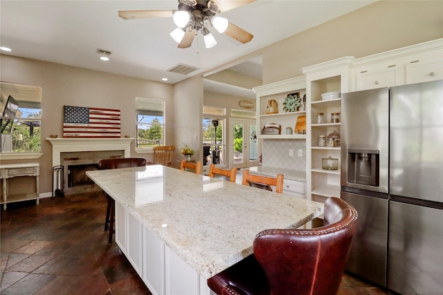 105 Sally Lake Ct, Angleton, TX 77515 - kitchen with stainless steel refrigerator with ice dispenser, a ceiling fan, white cabinets, light stone countertops, and a kitchen bar