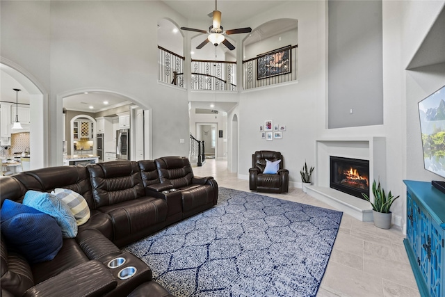 1002 Pleasant Pines Ln, Pinehurst, TX 77362 - living room featuring a ceiling fan, arched walkways, a glass covered fireplace, and a high ceiling