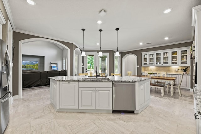 1002 Pleasant Pines Ln, Pinehurst, TX 77362 - kitchen with appliances with stainless steel finishes, arched walkways, white cabinets, a center island with sink, and ornamental molding