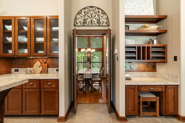 15608 Queen Victoria Ct, Montgomery, TX 77316 - kitchen with open shelves, glass insert cabinets, light stone countertops, brown cabinets, and a chandelier