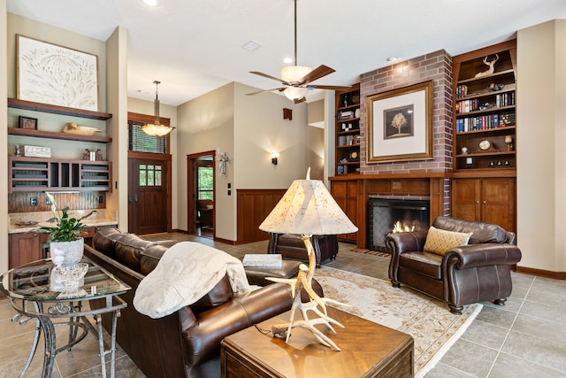 15608 Queen Victoria Ct, Montgomery, TX 77316 - living room with built in features, a brick fireplace, a ceiling fan, a wainscoted wall, and light tile patterned flooring
