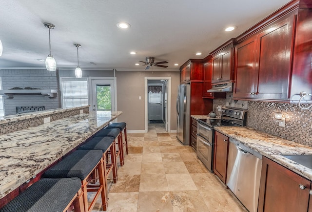 410 Shadywood Cir, Conroe, TX 77304 - kitchen with appliances with stainless steel finishes, under cabinet range hood, reddish brown cabinets, tasteful backsplash, and recessed lighting