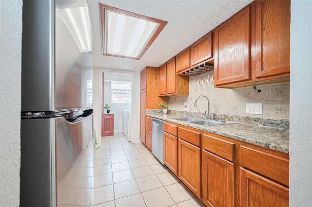511 Walston Ln, Houston, TX 77060 - kitchen featuring stainless steel appliances, brown cabinetry, light tile patterned floors, separate washer and dryer, and a textured ceiling