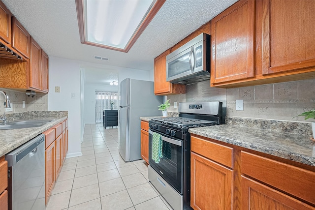 511 Walston Ln, Houston, TX 77060 - kitchen with stainless steel appliances, light tile patterned flooring, decorative backsplash, brown cabinetry, and a textured ceiling