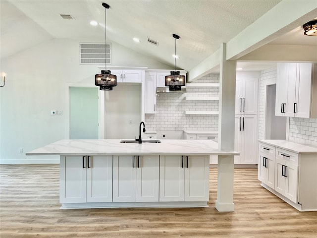 5030 Glenvalley Dr, La Porte, TX 77571 - kitchen with light wood-type flooring, an island with sink, vaulted ceiling, white cabinetry, and decorative backsplash