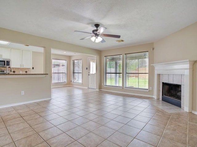 26610 W Surrey Park Ln W, Katy, TX 77494 - unfurnished living room featuring light tile patterned floors, ceiling fan, a tile fireplace, and a textured ceiling