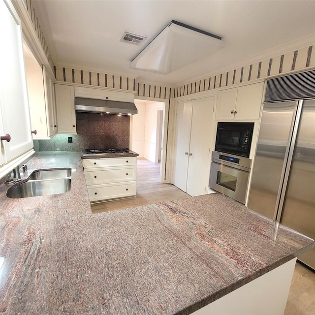 5227 Imogene St, Houston, TX 77096 - kitchen featuring appliances with stainless steel finishes, exhaust hood, dark stone countertops, white cabinets, and tasteful backsplash